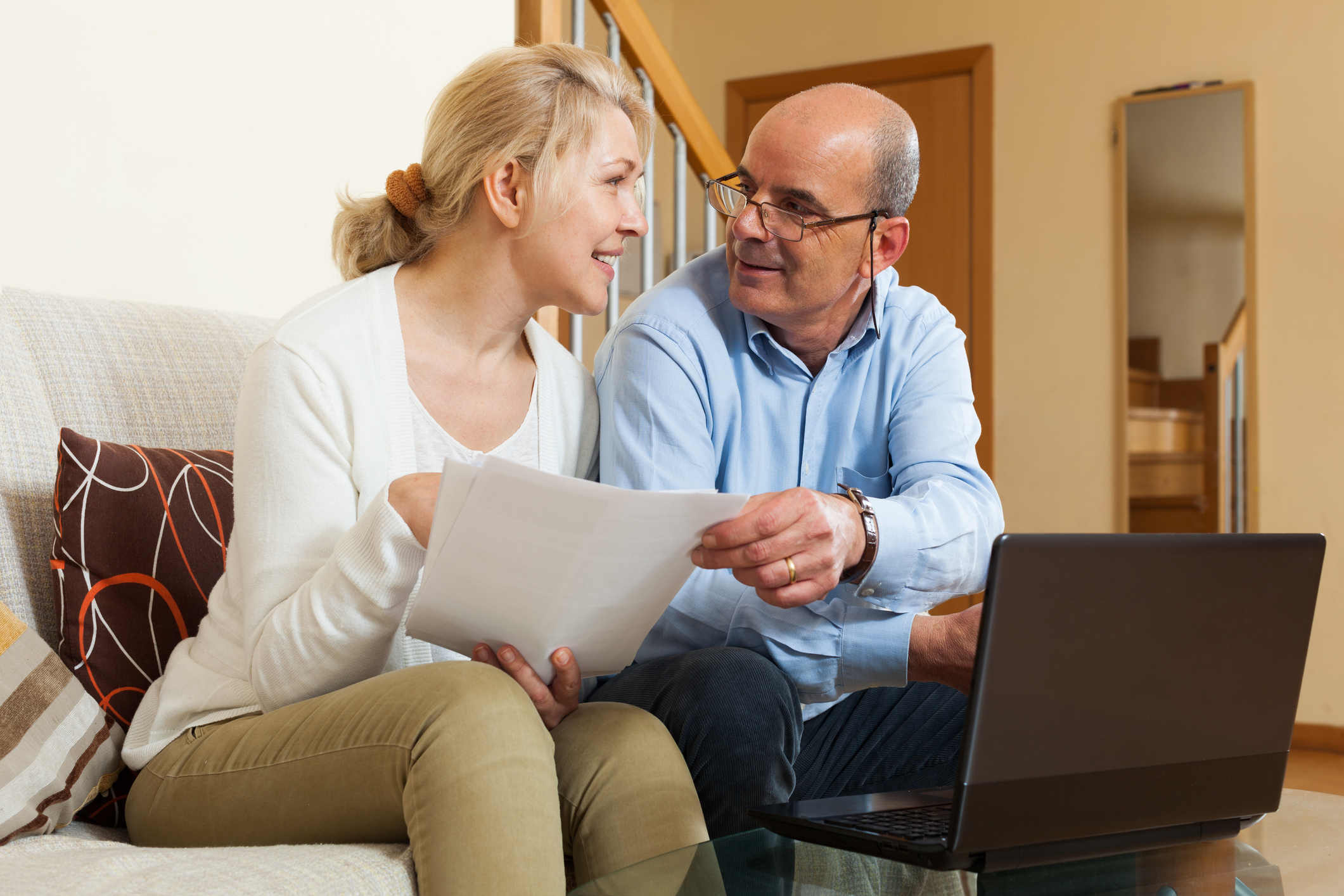 Smiling senior mature couple with financial documents and laptop in home